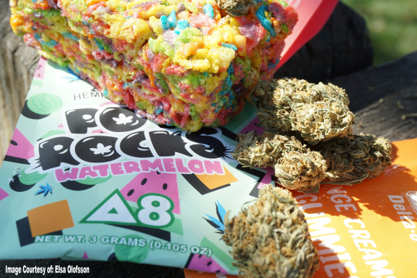 A colorful Delta-8 THC edible treat with vibrant cereal pieces sits on top of watermelon-flavored Pop Rocks packaging, next to several cannabis buds on an orange Delta-8 gummy wrapper. Image courtesy of Elsa Olofsson.
